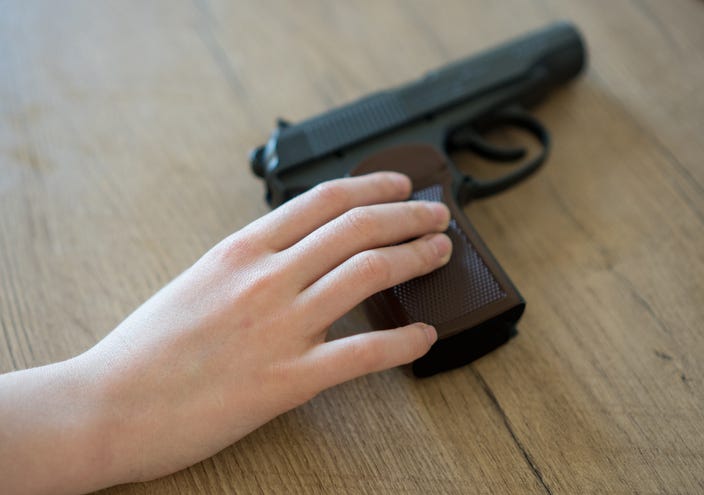 Child hand taking pistol from a table.