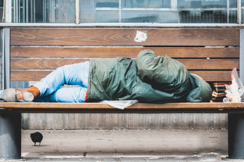 A homeless man sleeps on a bench