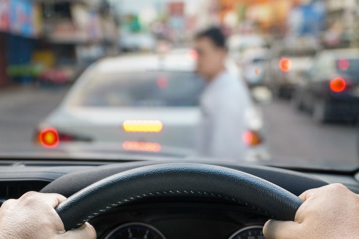 Point of view shot of a driver looking through the windshield. A pedestrian is walking in front of his car. The view outside of the windshield is blurred for effect.