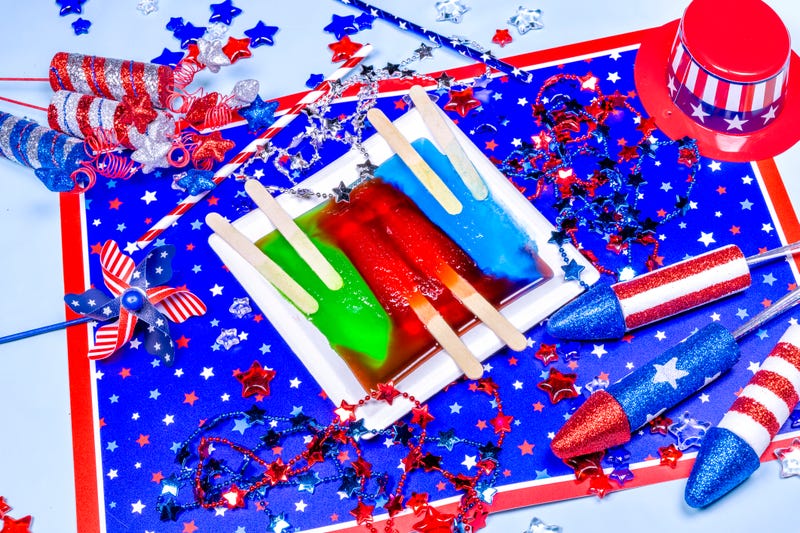 Three popsicles on a white plate melting against a colorful American patriotic backdrop celebrating July fourth and Memorial Day.