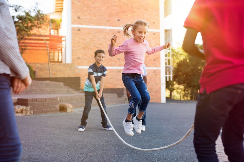 Happy elementary kids playing together with jumping rope outdoor. Children playing skipping rope jumping game and laughing outdoors. .