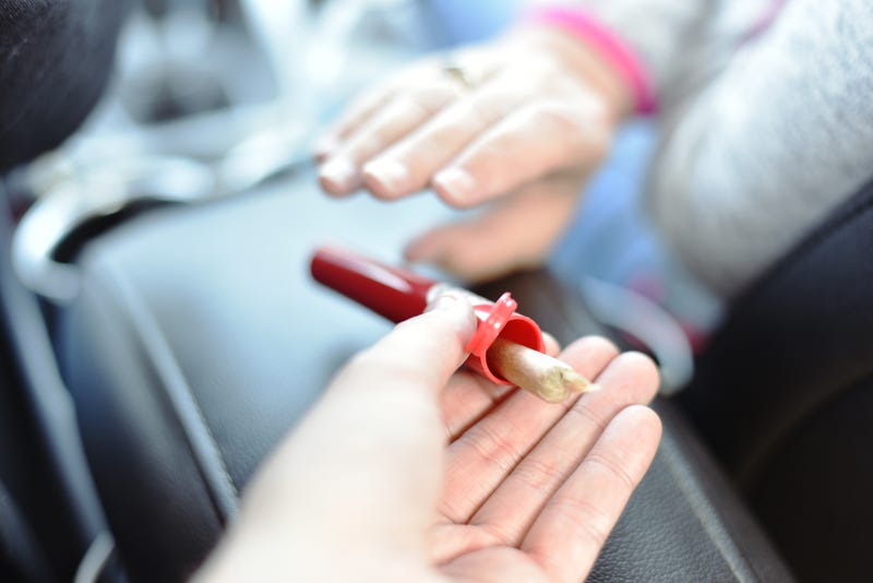Hand reaching for another hand holding pre rolled cannabis joint inside car.