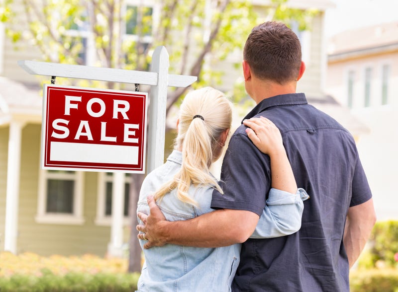 Couple Facing Front of Sold Real Estate Sign and House