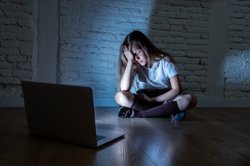 Girl sitting sadly against a wall after getting bullied online