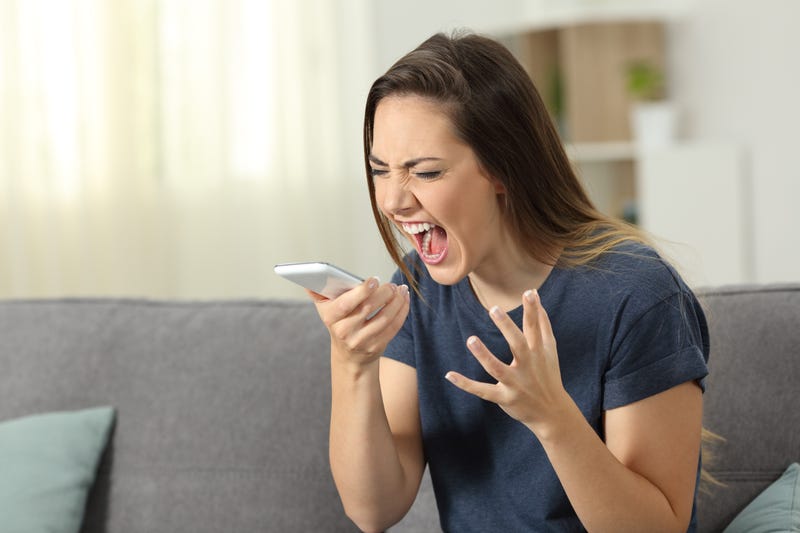 Furious woman shouting to smart phone sitting on a couch in the living room at home