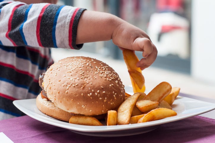 little boy hand eating hamburger and french fries