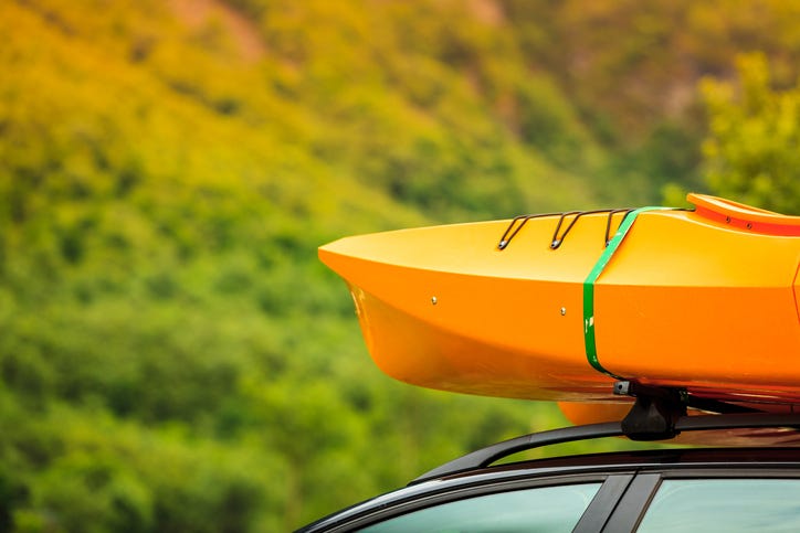 Close up of a kayak on the top of a vehicle in a forested area.