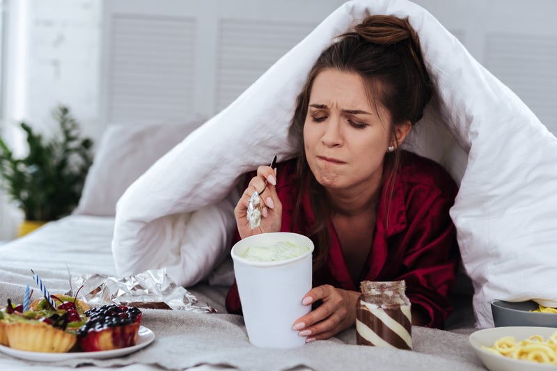 woman hiding under a blanket eating ice cream out of a carton