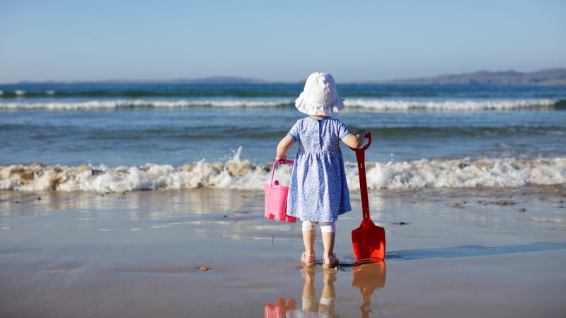 Toddler on the beach with a sun hat, a shovel, and a bucket
