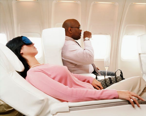 Woman reclined in airplane seat while man sitting next to her takes a drink