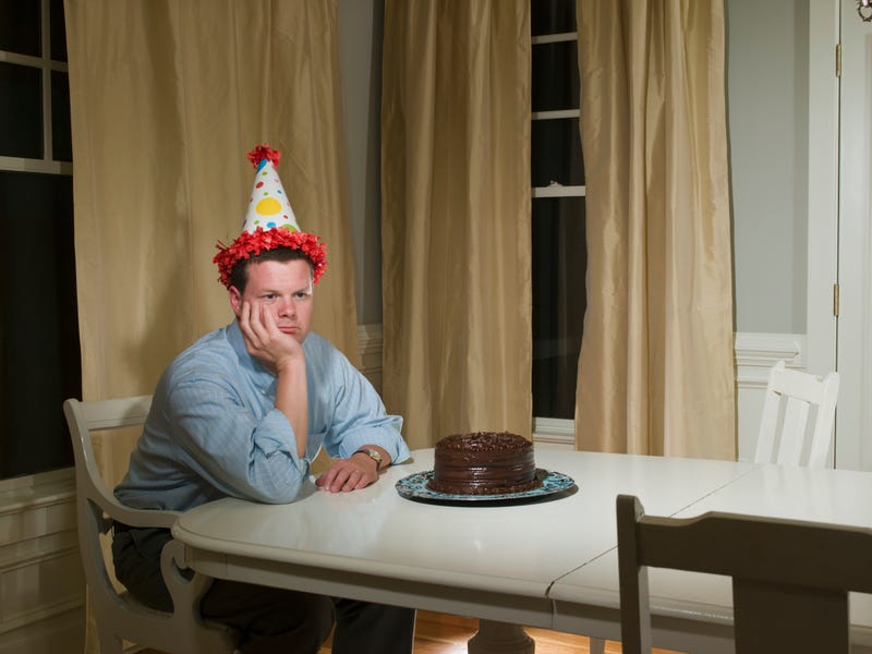 Mid adult man in party hat, sitting at table in front of birthday cake - stock photo