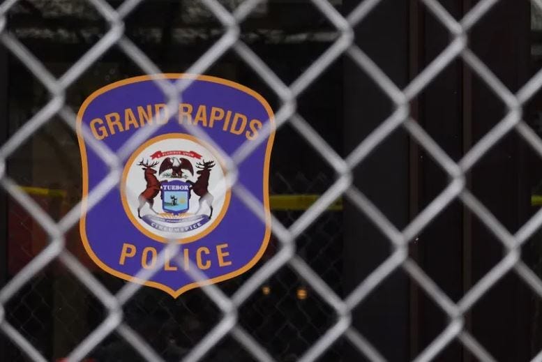 Police badge logo for Grand Rapids Police Department, viewed through a chain link fence.