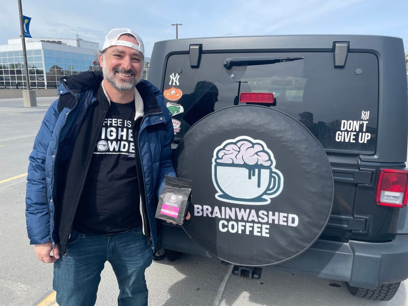 Magner stands with a bag of Brainwashed Coffee beans in front of the branded decal on his car.