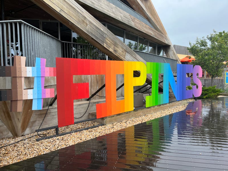 A sign for the Fire Island Pines decked out in the colors of the rainbow greets you at the ferry dock