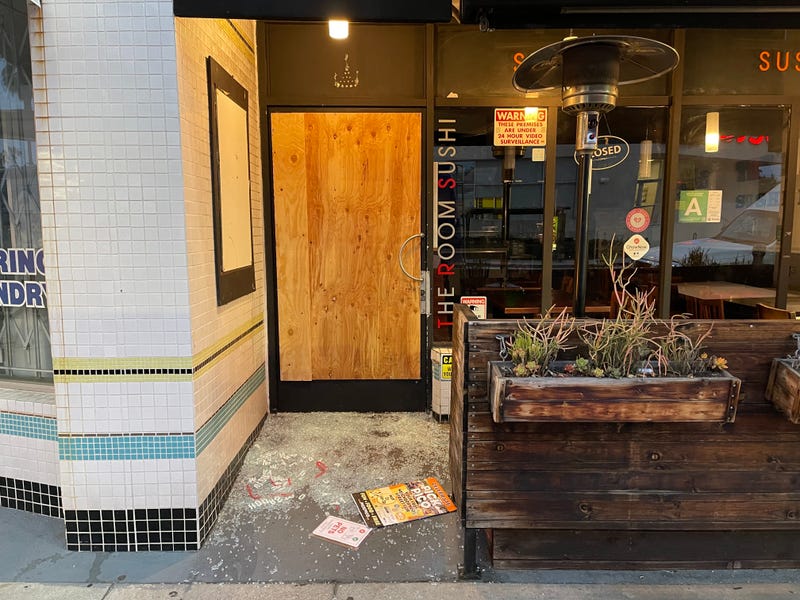 boarded up door of a business with glass shards outside