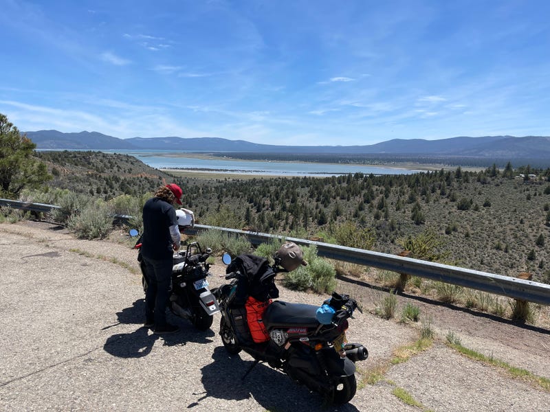 two guys riding scooters in the middle of nowhere
