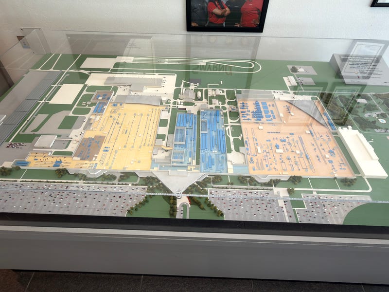 An architectural model of an extensive factory floor plan under glass, featuring sections in yellow, blue, and beige, set on a green layout base.