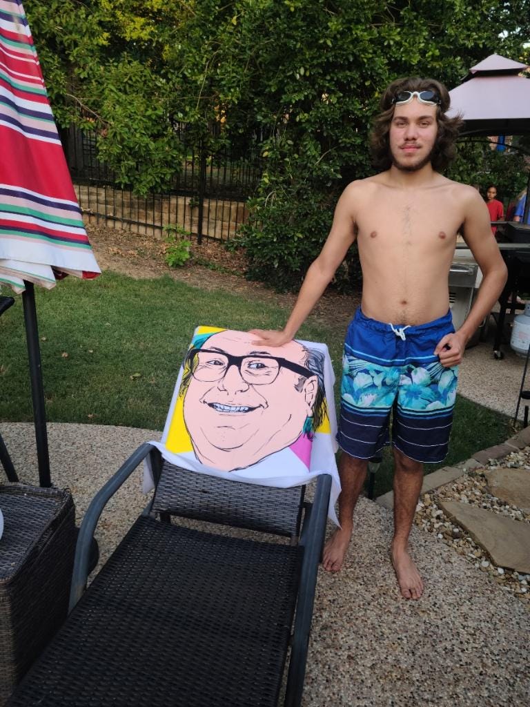 Dylan Dorrell proudly displays a unique beach towel sporting the face of Danny’s DeVito.
