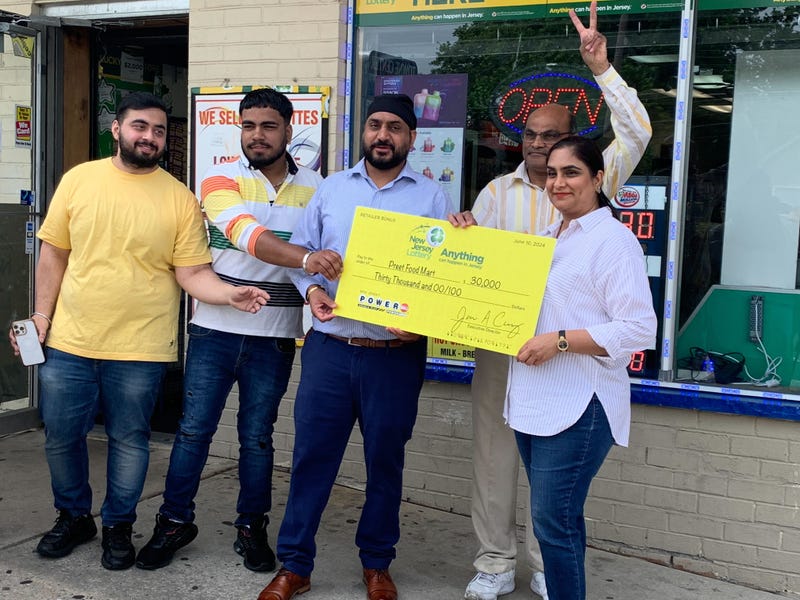 From left: Two employees, Tony Singh, Harish Patel and Raj Singh hold up a check their store received for selling a $221 million winning Powerball jackpot ticket, June 11, 2024.