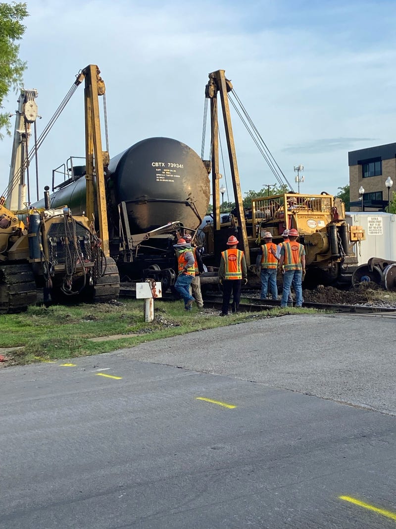 Crews use a crane to right a derailed tanker car