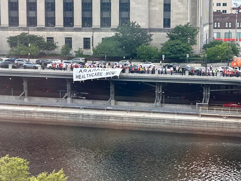 Striking workers unfurled a banner reading "Aramark health care now" and hung it over the Schuylkill Avenue guardrail, across the river from Aramark's corporate headquarters.