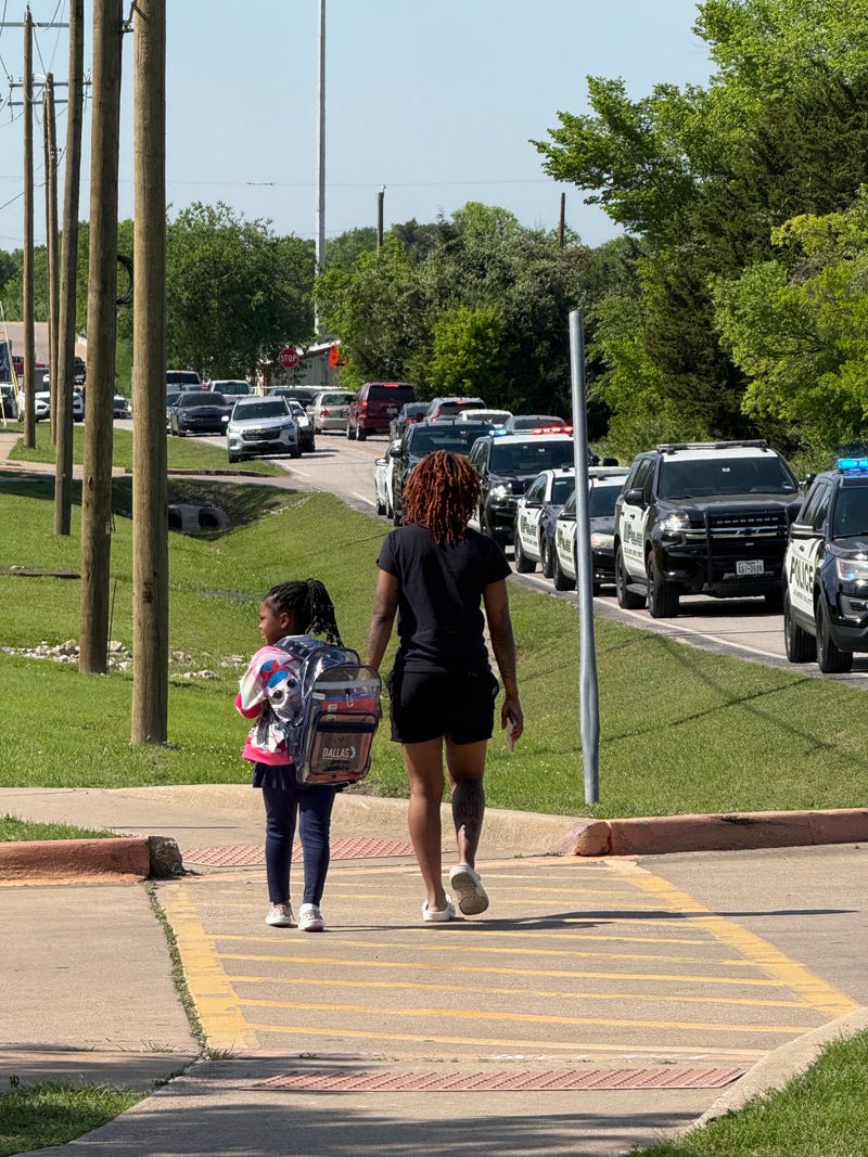 A mom and her daughter walk past the crime scene at Wilmer Hutchins High School Tuesday