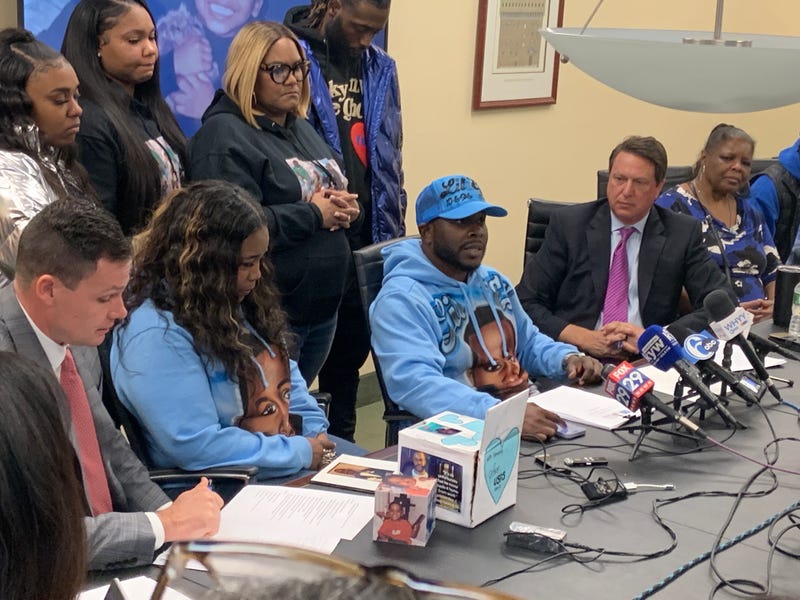 Dawn Fobbs (second from left, seated) and Eric Coates (center, seated), along with attorney Eric Zajac (second from right), address media about their civil lawsuit against Macy's and its Center City location's building owners and management.