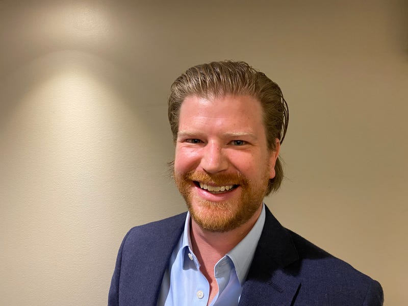 jack coatar. he's a white man with strawberry blond hair and beard and a blue shirt and suit jacket