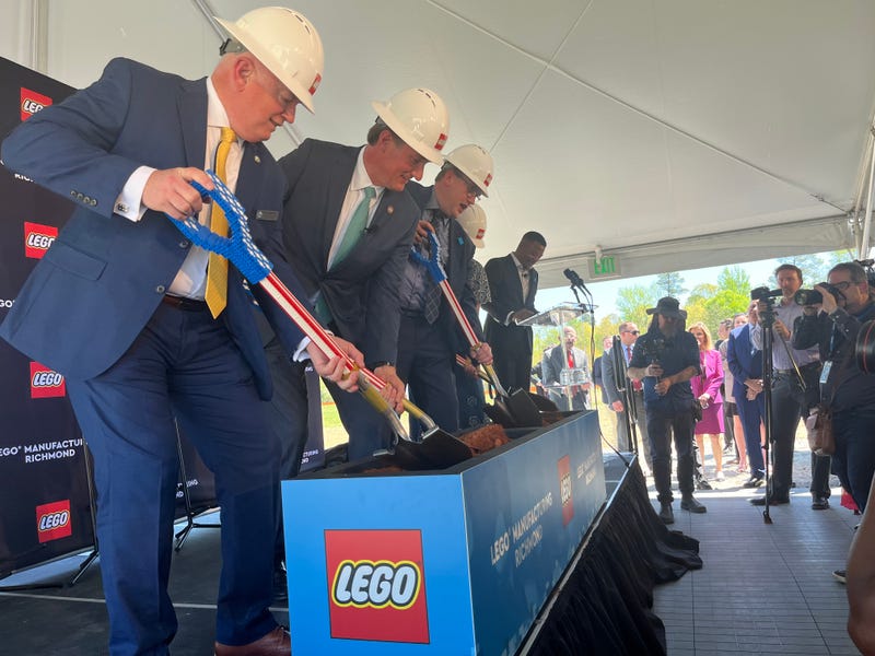 Several people stand in a line, wearing hard hats, digging