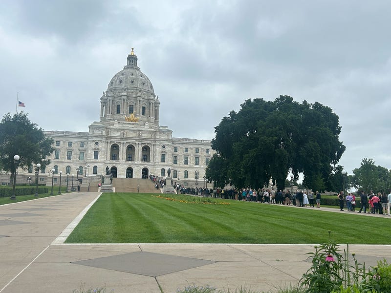 Flags atop Minnesota state capitol building fly at half-staff as Melissa Hortman, her husband and family dog, all lie in state with mourners already lined up well outside the rotunda.