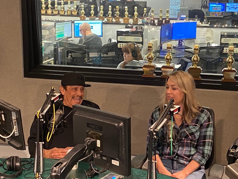 Danny Trejo sits down in the KNX radio studio wearing a black shirt and a black hat.