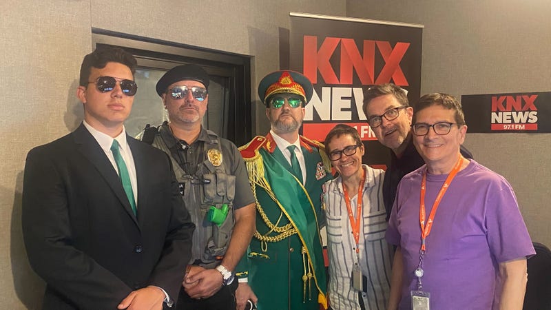 man in regal garb and two bodyguards with knx news anchors