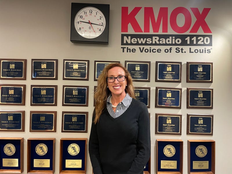 holly rehder stands in front of a kmox sign and awards