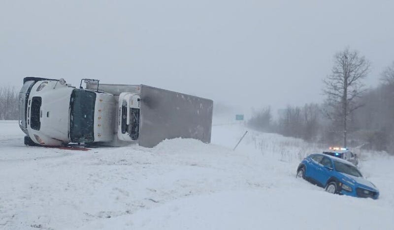 A semi lies on its side on a snow-covered stretch of northbound US-131. Another vehicle and a sheriff's patrol car are in the ditch on the side of the highway.