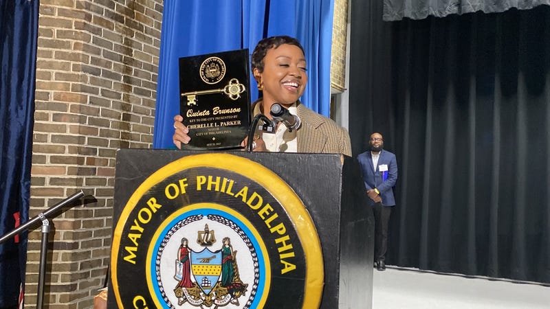 Quinta Brunson holds the key to the city standing at a podium with the mayor's seal.