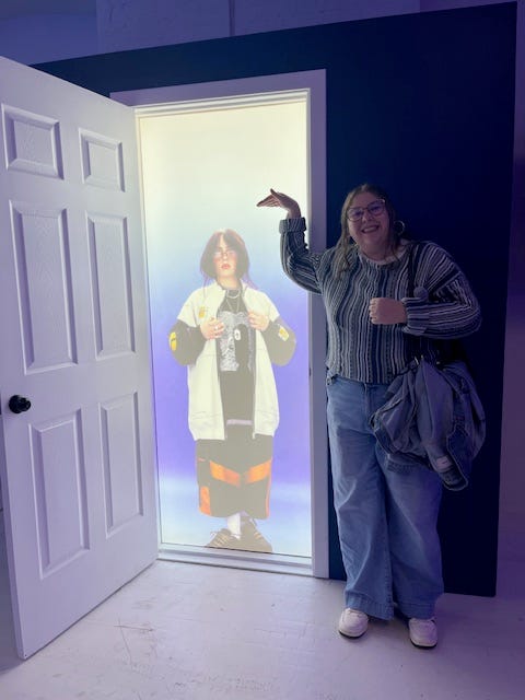 1010 WINS' Erin White next to a to-scale lit image of Billie Eilish at her pop-up photo opportunity in SoHo.