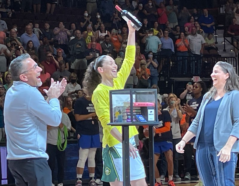 UConn basketball legend Sue Bird (at center) accepts a rack of books and a bottle of wine from the Connecticut Sun before her final game in Connecticut, at Mohegan Sun Arena, 7/28/22