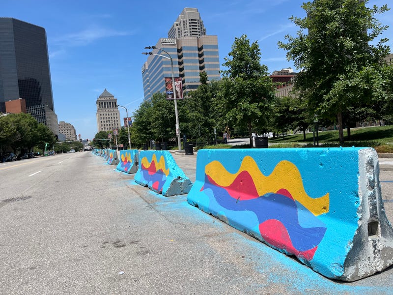 downtown barricades painted. the design is a light blue background with pink, purple and yellow wavy designs in the middle