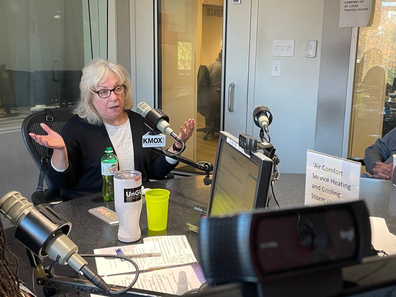 jo mannies sits at a microphone in the KMOX studios. she's a white woman with white hair and glasses