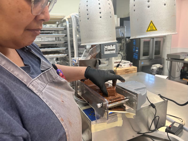 An employee uses a machine to cover marshmallows in chocolate. 