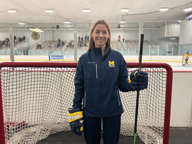 Hockey coach Erin Proctor stands in front of a hockey net and rink.