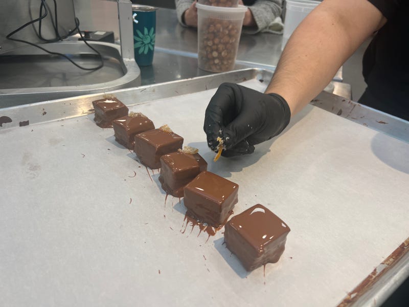 An employee adds a garnish to freshly coated chocolate covered marshmallows