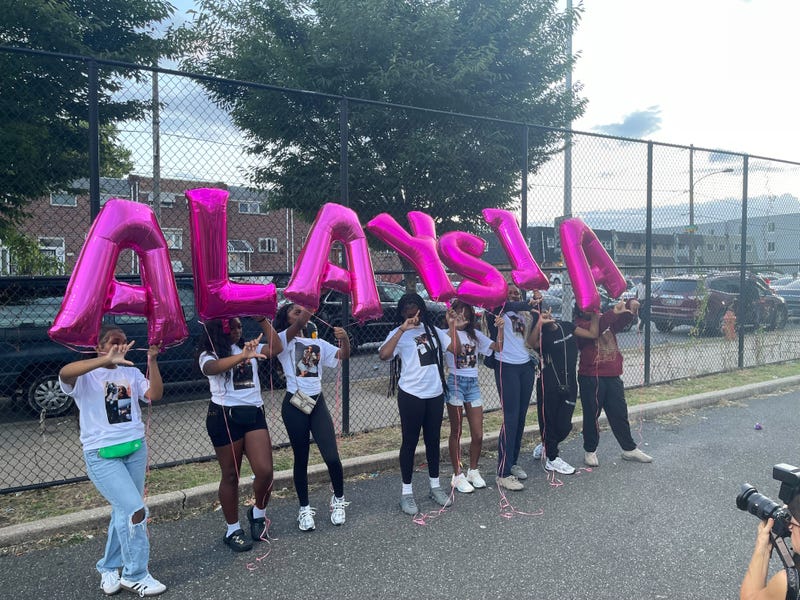 Cheer teammates of Alaysia Smith holding balloons spelling out her name.