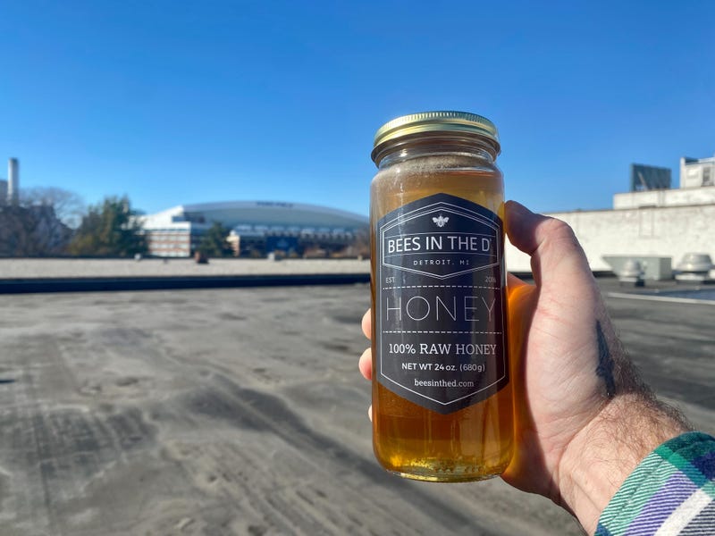 Hand holding jar of Bees in the D honey with Ford Field in the background