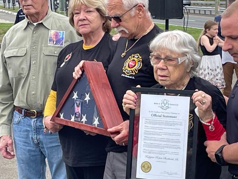 Steven Sharkevich (holding flag) and Sophia Sharkevich (holding letter of commendation) appear at a ceremony honoring firefighters who helped battle wildfires in Connecticut in 2024. The special honors were presented posthumously to Robert Sharkevich, Sr. (Steven's brother and Sophia's son).