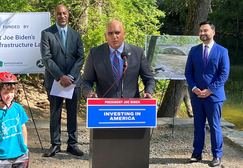 Federal Highway Administrator Shailen Bhatt (center) announces a $14.2 million federal grant to repair the historic Bells Mill Road and Valley Green Road bridges, along with Office of Transportation and Infrastructure Systems Managing Director Mike Carroll (left) and National Climate Advisor Ali Zaldi (right).