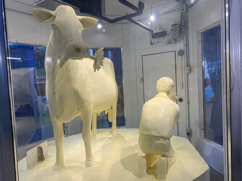 A cow holding a sunflower stands next to a farmer -- all made of butter.