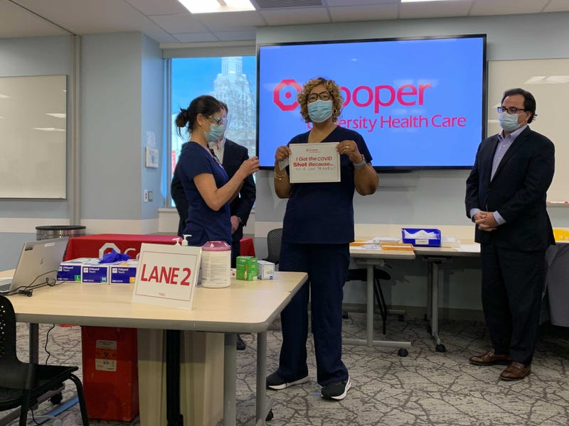 After getting the COVID-19 vaccine, nurse manager Rosetta Oliver holds up a sign reading: "I got the shot ... so I can travel!"