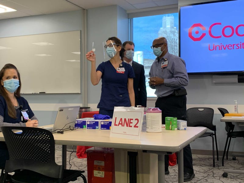 A Cooper nurse holds up a vial of the COVID-19 vaccine, as the third in line to get then shot, Dr. Guy Hewlett, stands by.