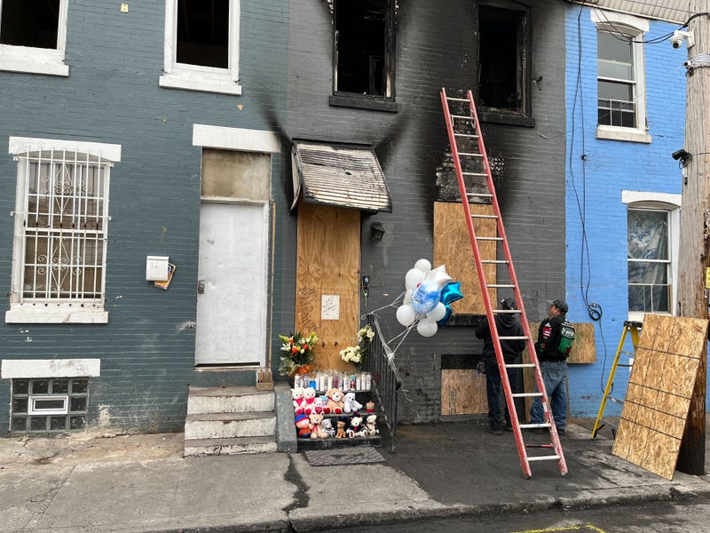 Two men board up the row house that caught fire on April 24, 2022, killing a father and his three children inside. The mother jumped out a second-story window and survived.